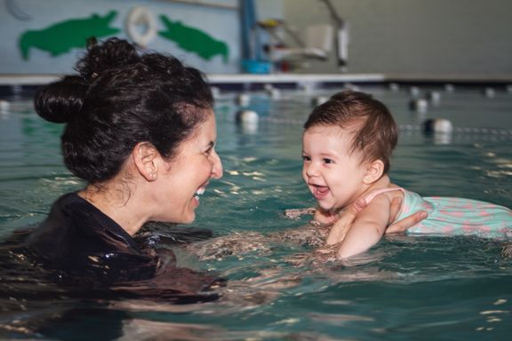 a woman is teaching a baby how to swim in a swimming pool and smiling .