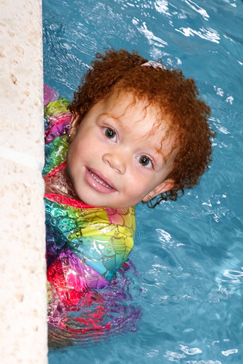 a little girl with red hair is swimming in a pool for a swim school