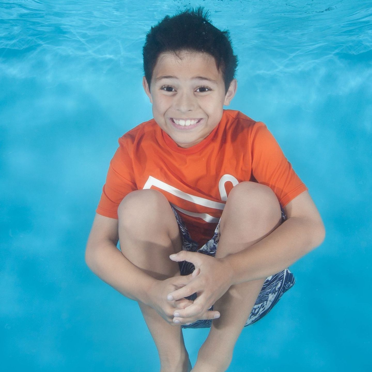 a young boy in an orange shirt is swimming under water during swim lessons