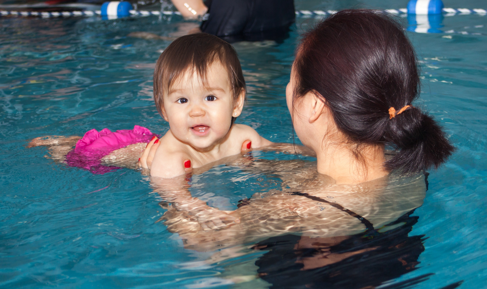 a woman is holding a baby in a swimming pool enjoying fun swim lessons