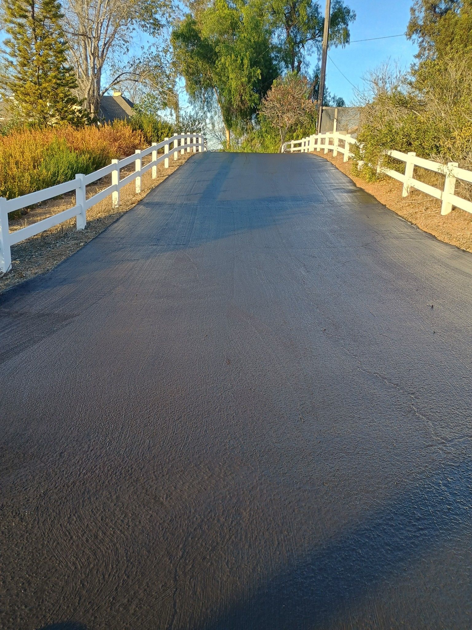 A black road with a white fence on the side of it.