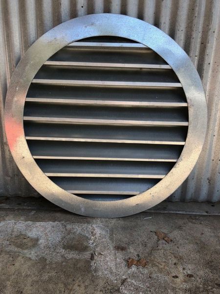 A round metal grille is sitting on the ground in front of a metal wall.