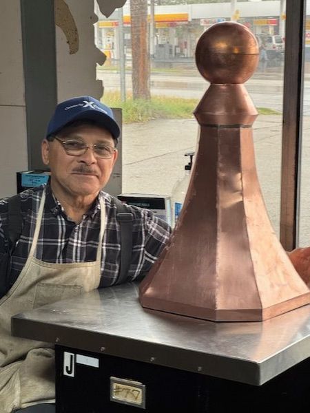 A man is standing next to a large copper chess piece on a table.