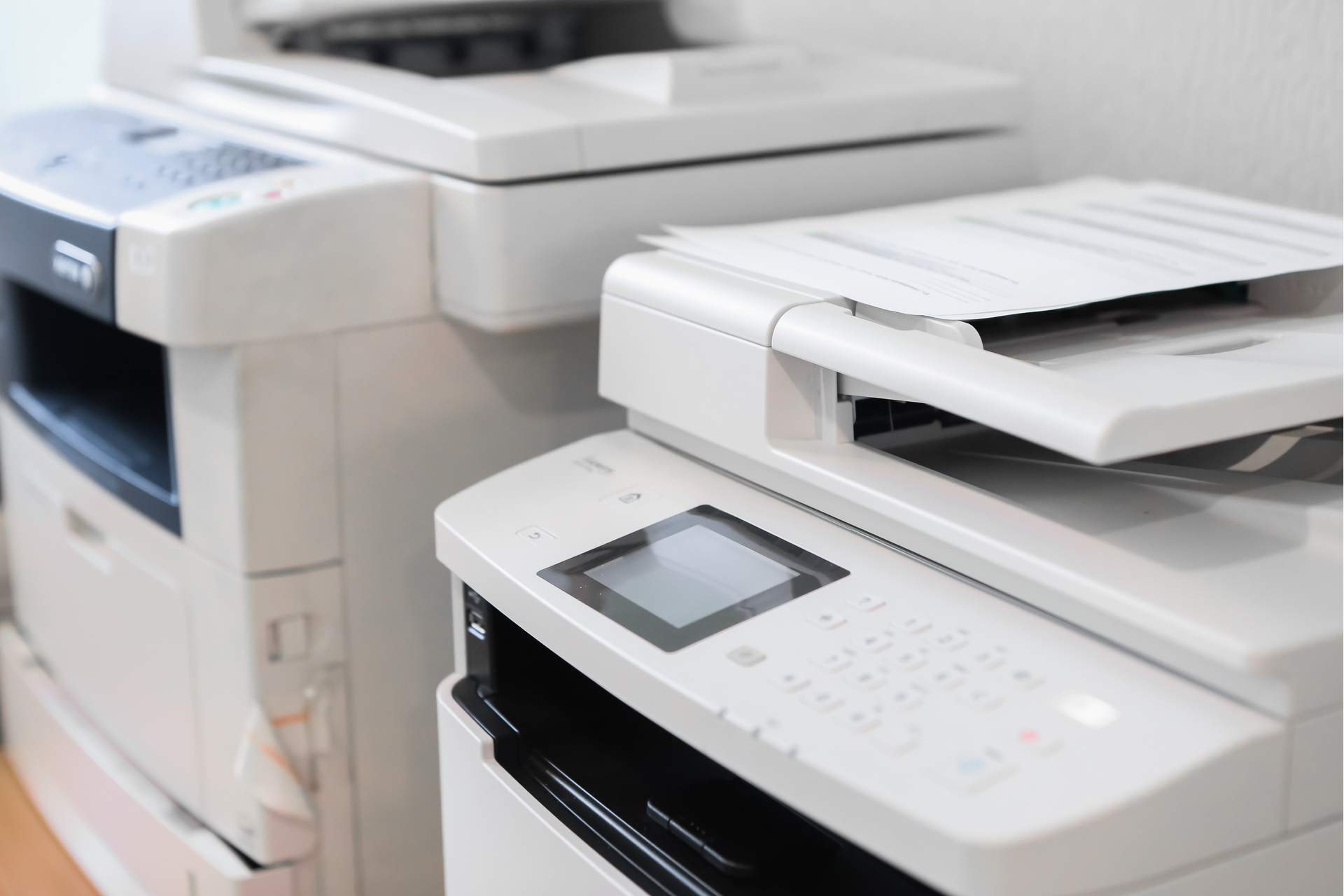 A professional woman is crouching in front of a copier machine, adjusting or replacing a toner cartr