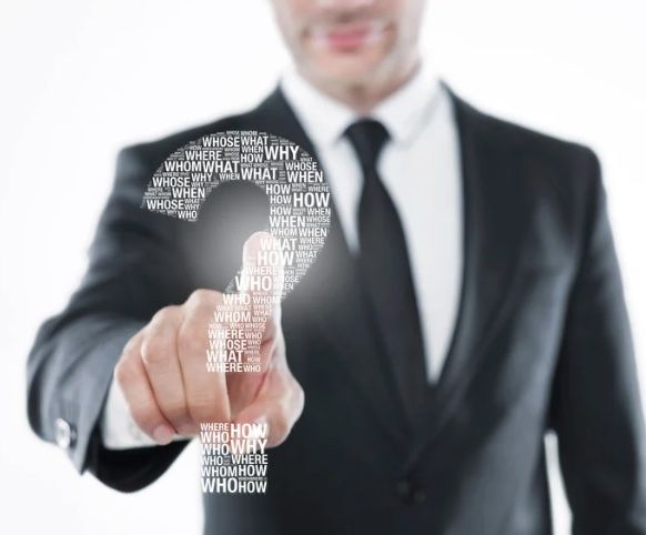 Man in suit pointing at a question mark made of words, possibly exploring ideas.