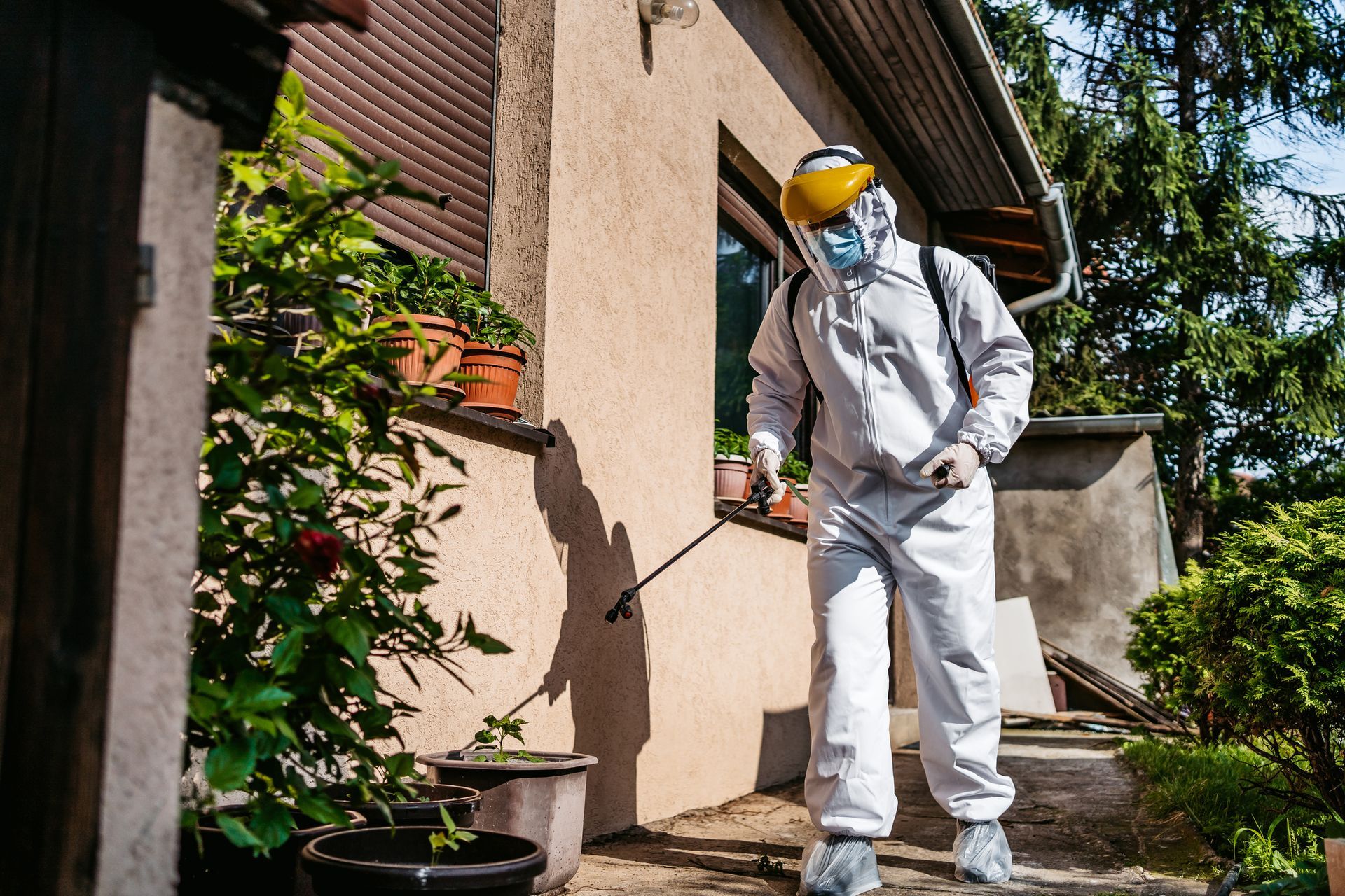 A man in a protective suit is spraying a house with a sprayer.