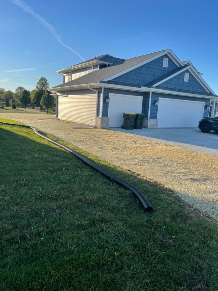 A house with a blue exterior and white garage doors, black drainage pipe on the green grass.