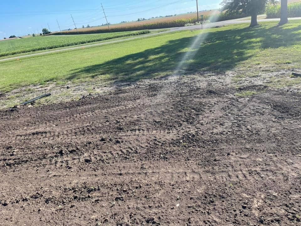 Muddy ground with tire tracks, green grass, and a road under a bright sky.