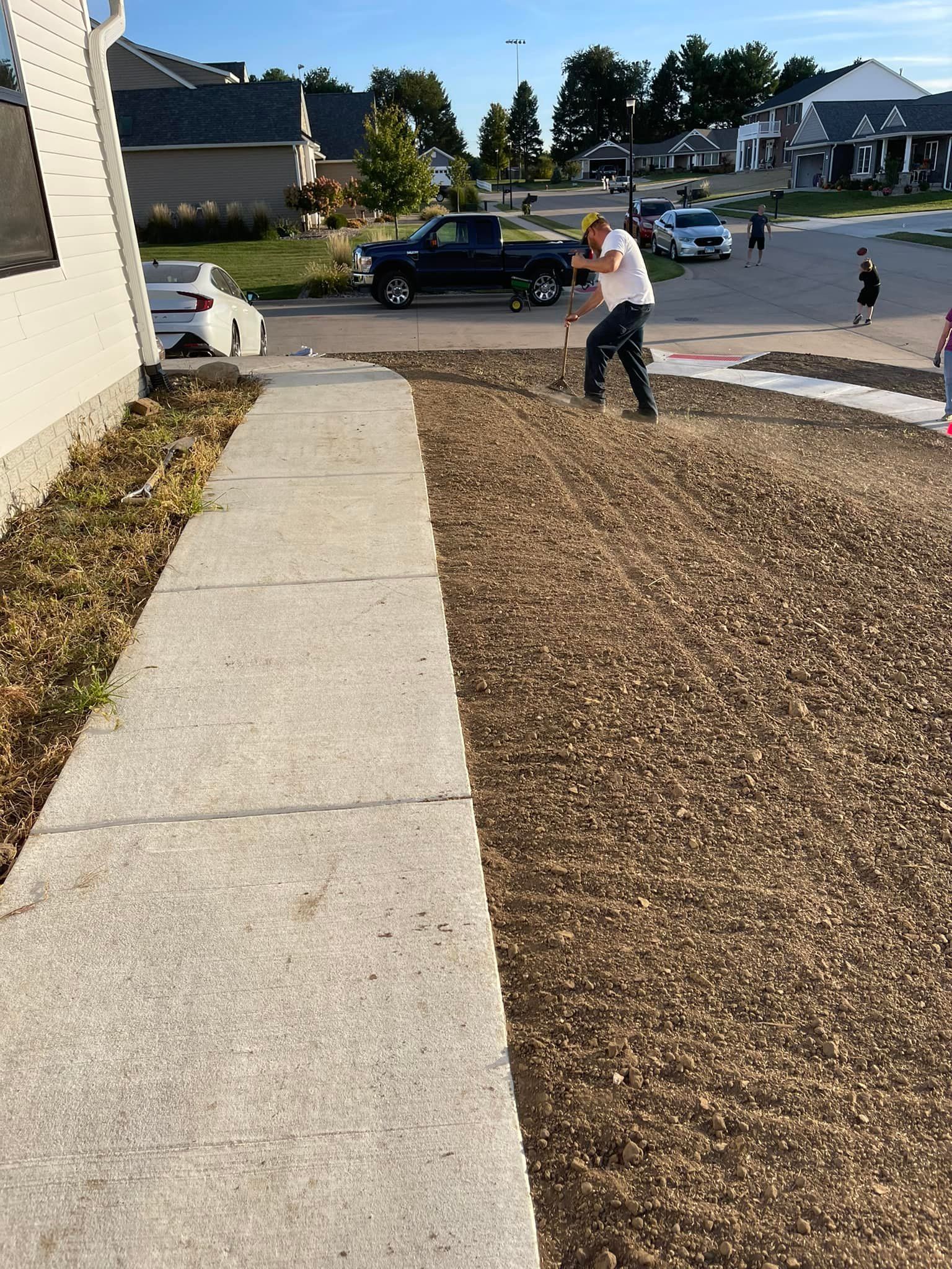 Man raking a newly seeded lawn next to a sidewalk and house.