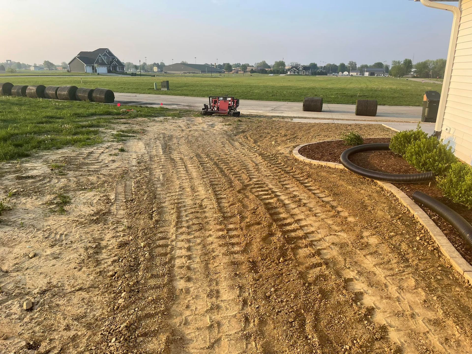 Dirt yard with tire tracks, small red tractor, and new landscaping border.