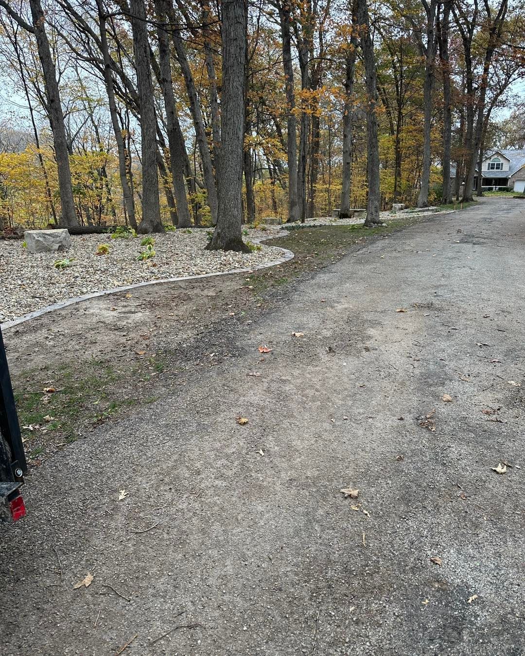 Gravel driveway curves past a treeline with autumn foliage. A house is visible in the background.