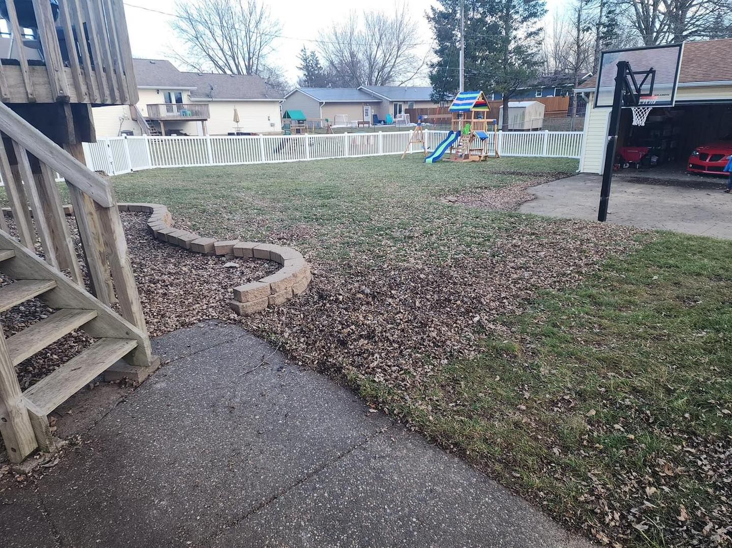 Backyard with fallen leaves, a fence, a basketball hoop, and a play structure.