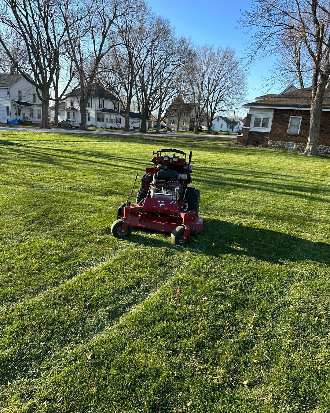 Red lawn mower cutting grass in a residential yard. Buildings in background.