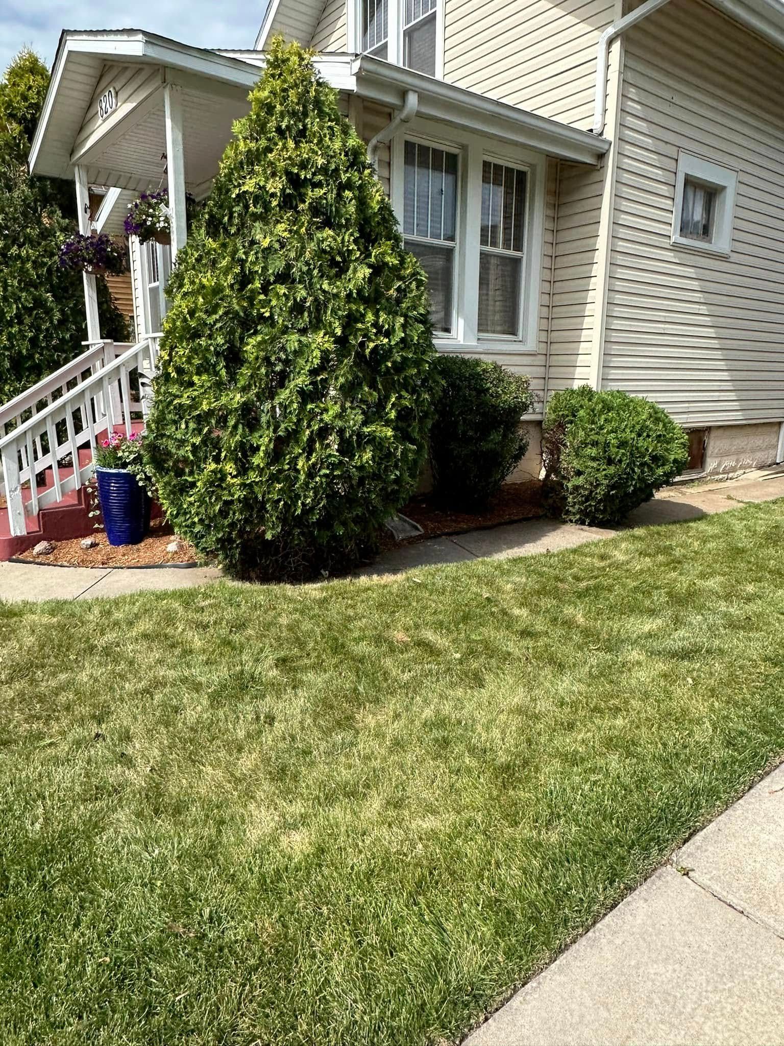 Exterior of a light-colored house with a porch, bushes, and a lawn.