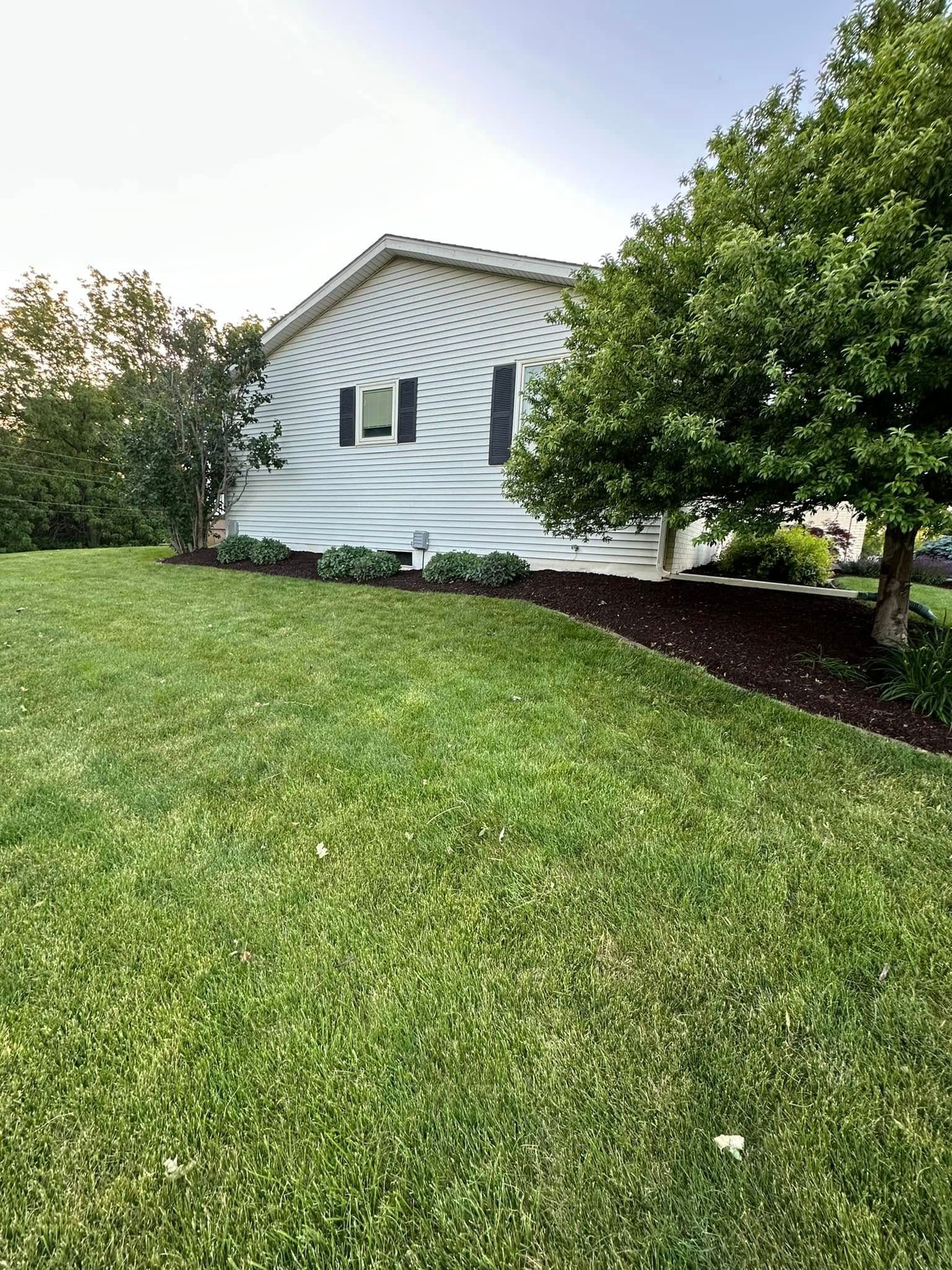 White house with wavy siding, black shutters, and trees on a green lawn.