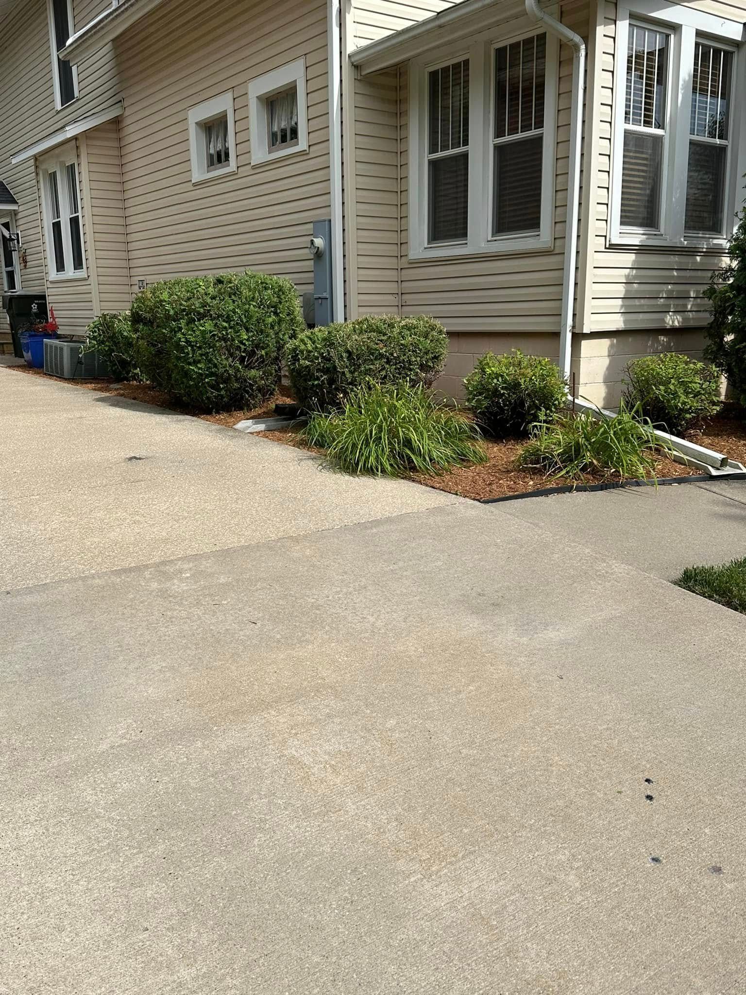 Sidewalk next to a beige house with small green bushes along the foundation.
