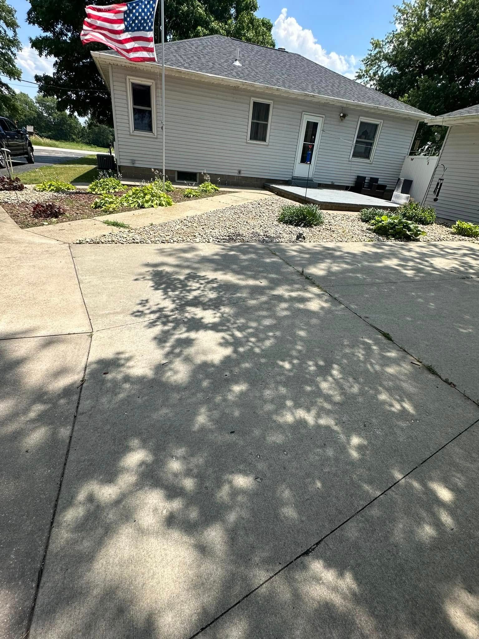 A residential house with a driveway. An American flag flies. Sunlight casts shadows on the concrete.