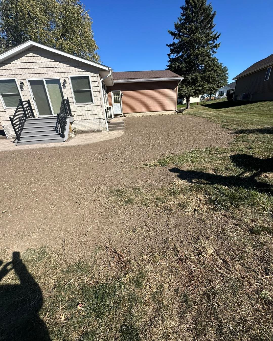 Gravel driveway next to a house with a stone facade, garage, and patchy grass under a blue sky.