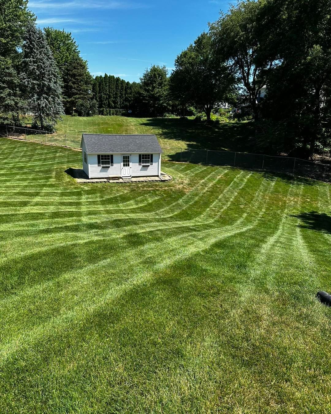 White shed in a green field with striped mowing pattern; sunny day.