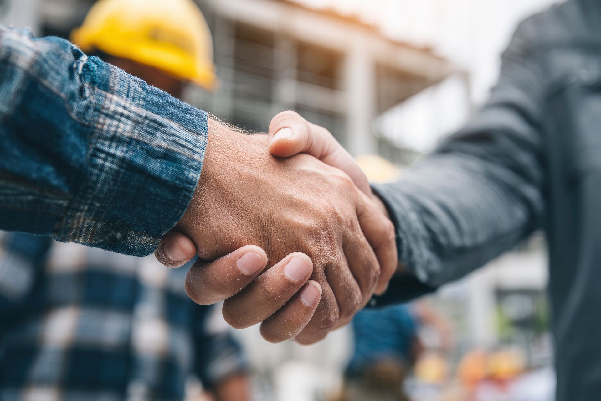 Zwei Personen in Arbeitskleidung schütteln sich auf einer Baustelle die Hände.