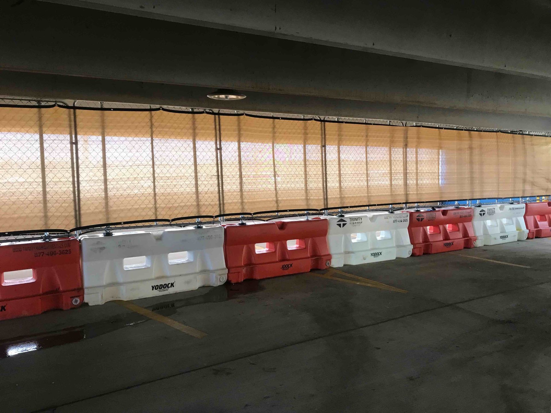 Fence panels on top of a row of red , white water filled barriers
