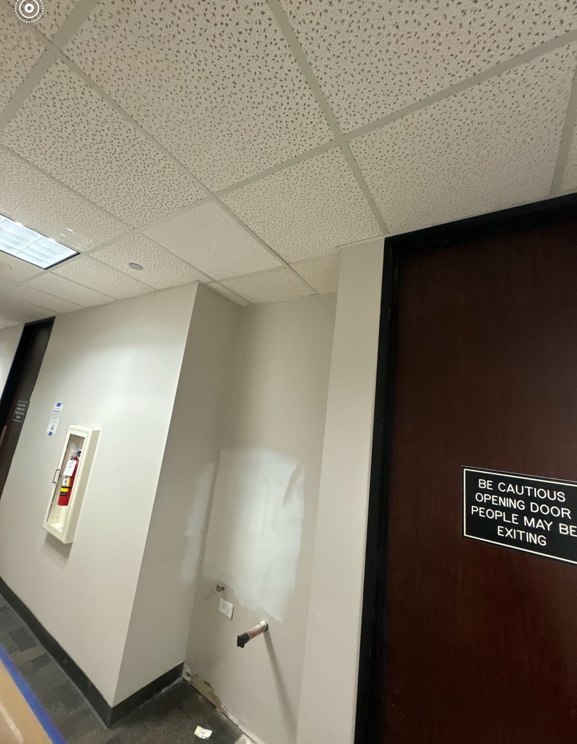 A hallway with a fire extinguisher on the wall and a sign on the door.