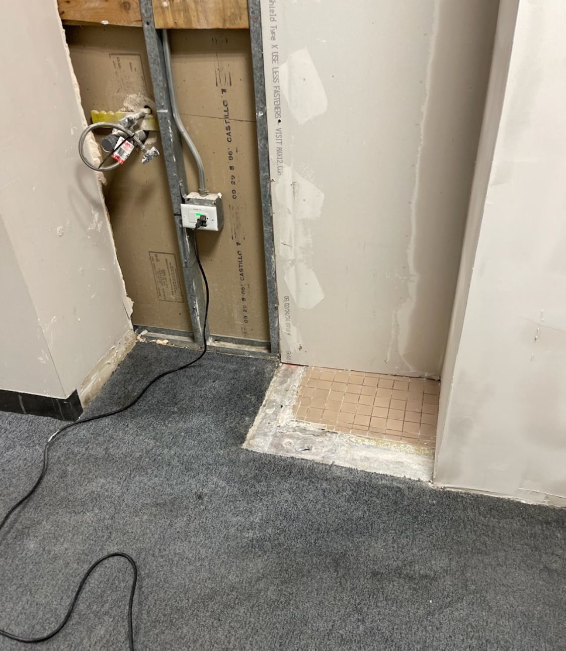 A room with a carpeted floor and a wall with electrical wires coming out of it.