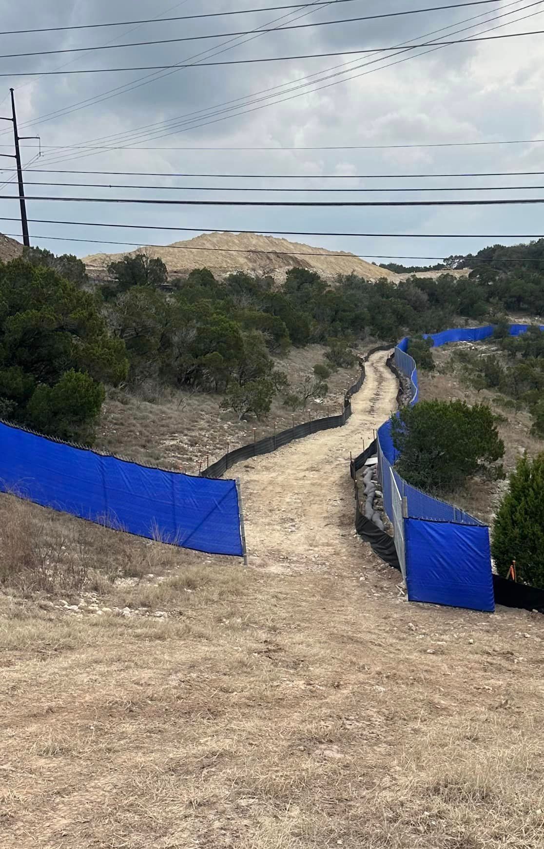 A dirt road with a blue fence along the side of it.