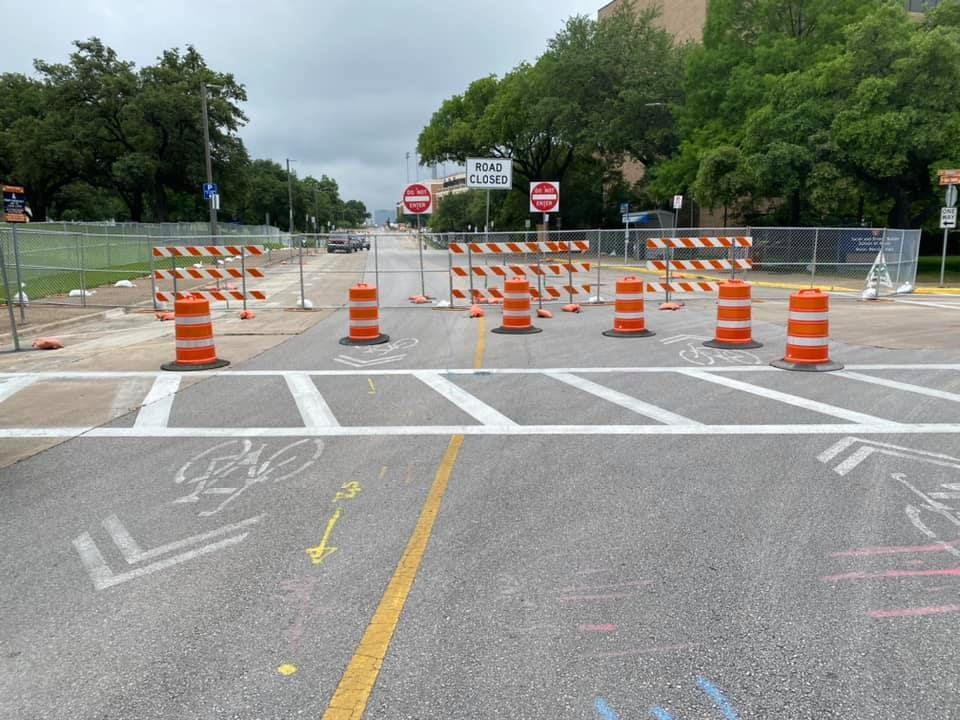 A construction site with a bicycle lane and orange traffic control barrels on the side of the road.