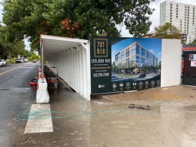 A construction site with a large billboard beside a safety pedestrian walkway.