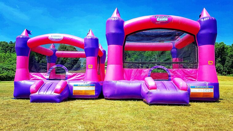 A pink and purple bouncy house is sitting on top of a lush green field.
