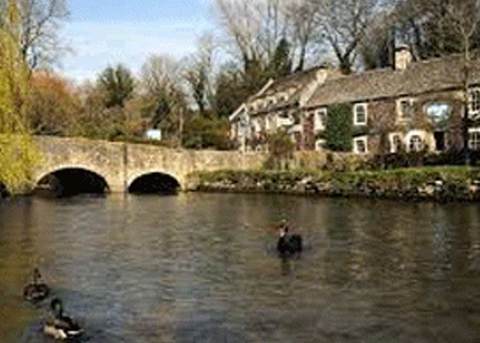 A bridge over a river with ducks in the water and a house in the background.