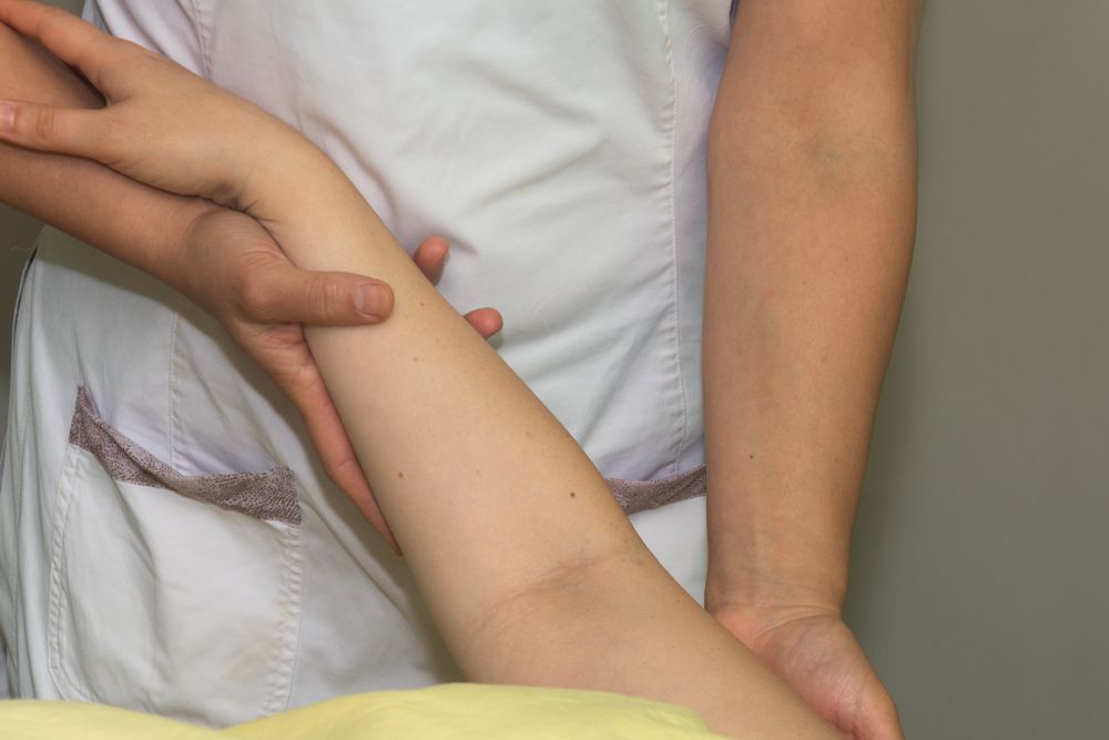 Person's lymphedemic arm being held by another, for a medical examination, indoors.