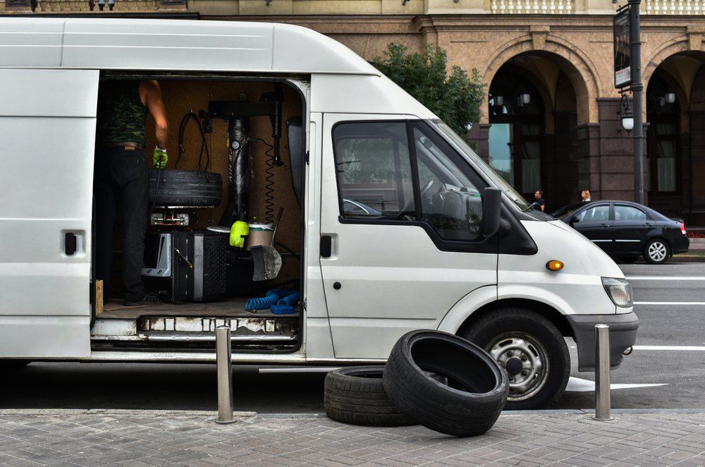 A White Van With Tires in the Back is Parked on the Side of the Road — Coffs Coast Mobile Mechanical in Toormina, NSW
