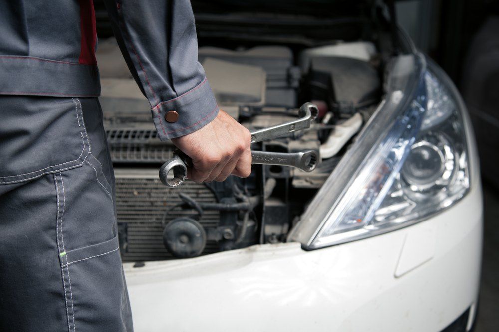 A Mechanic is Holding a Wrench in Front of a Car With the Hood Open — Coffs Coast Mobile Mechanical in Coffs Coast, NSW