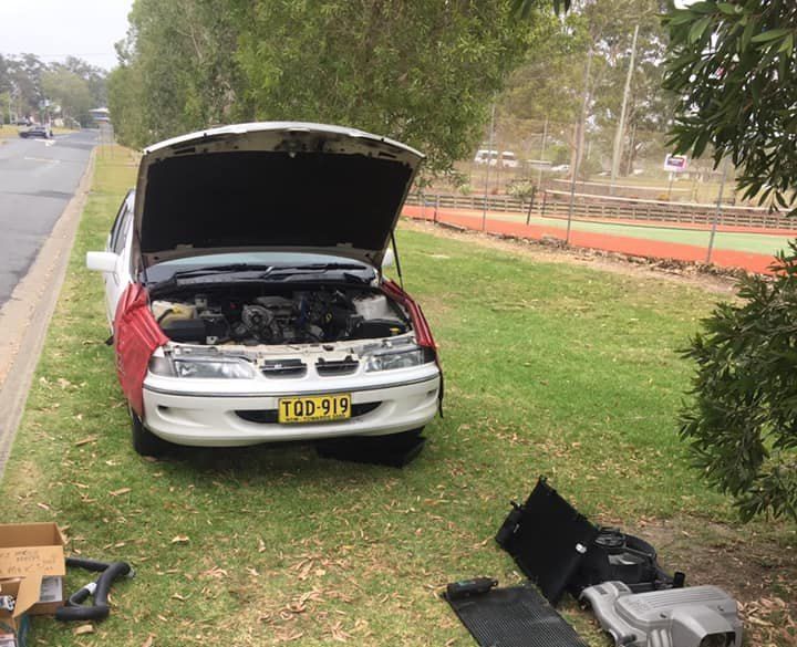 A Red and White Car With the Hood Up is Parked in the Grass — Coffs Coast Mobile Mechanical in Toormina, NSW