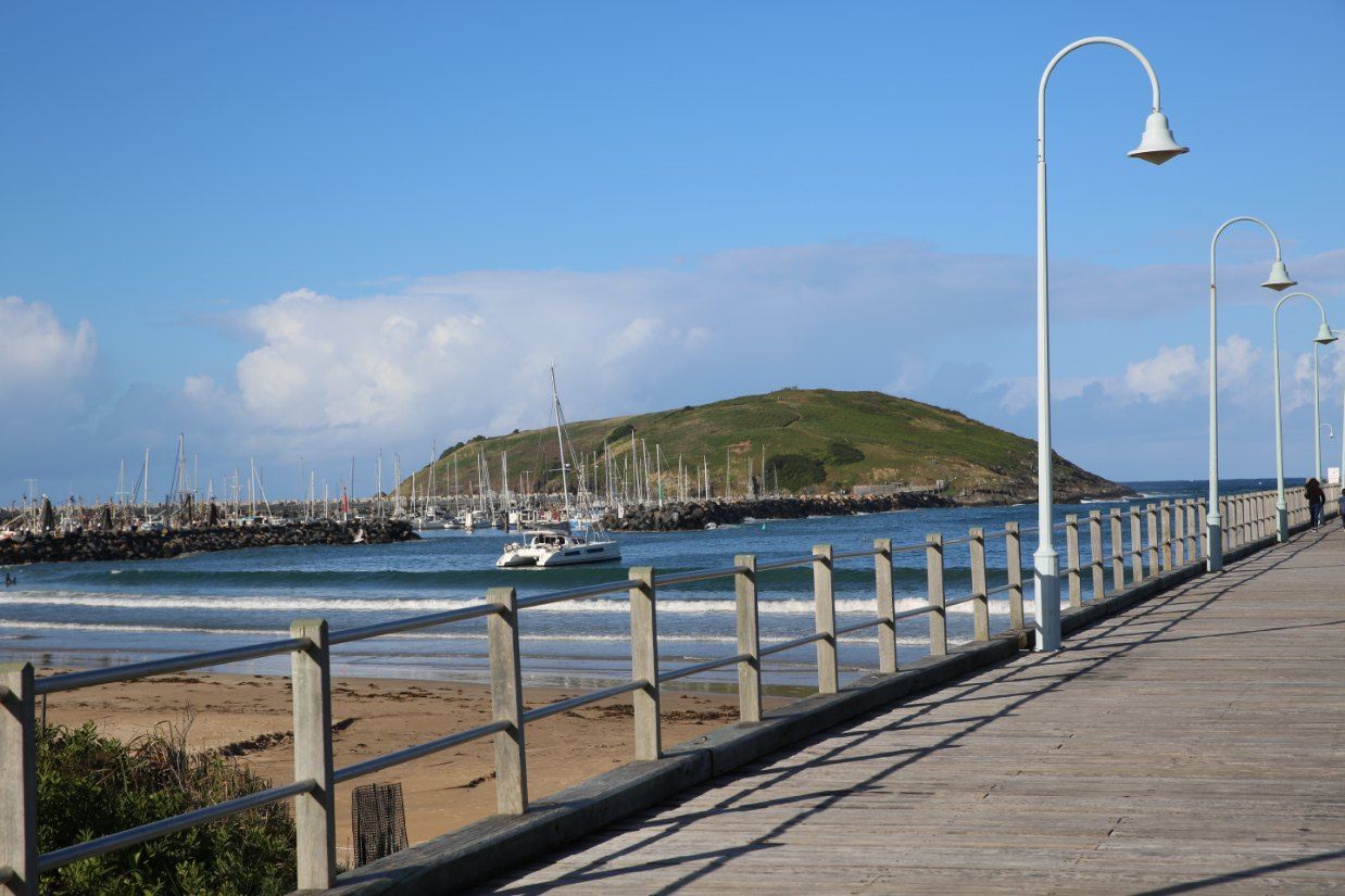 A Pier Leading to a Body of Water With a Boat in the Distance — Coffs Coast Mobile Mechanical in Coffs Coast, NSW