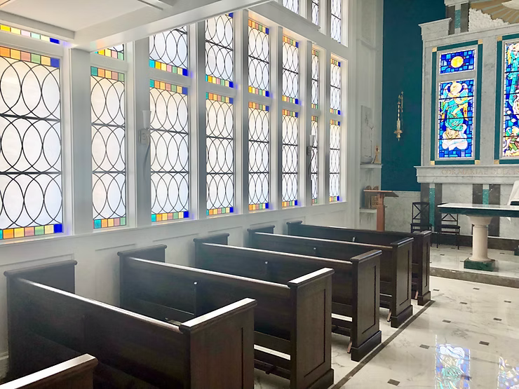 Interior view of a chapel with stained-glass windows, wooden pews, and marble flooring.