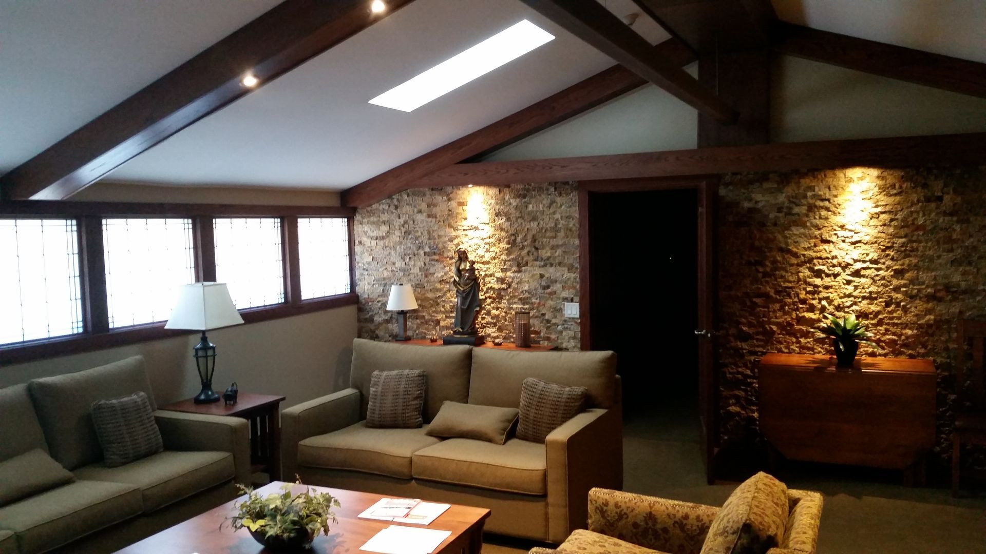 Living room with stone accent wall, skylight, wooden beams, and seating.