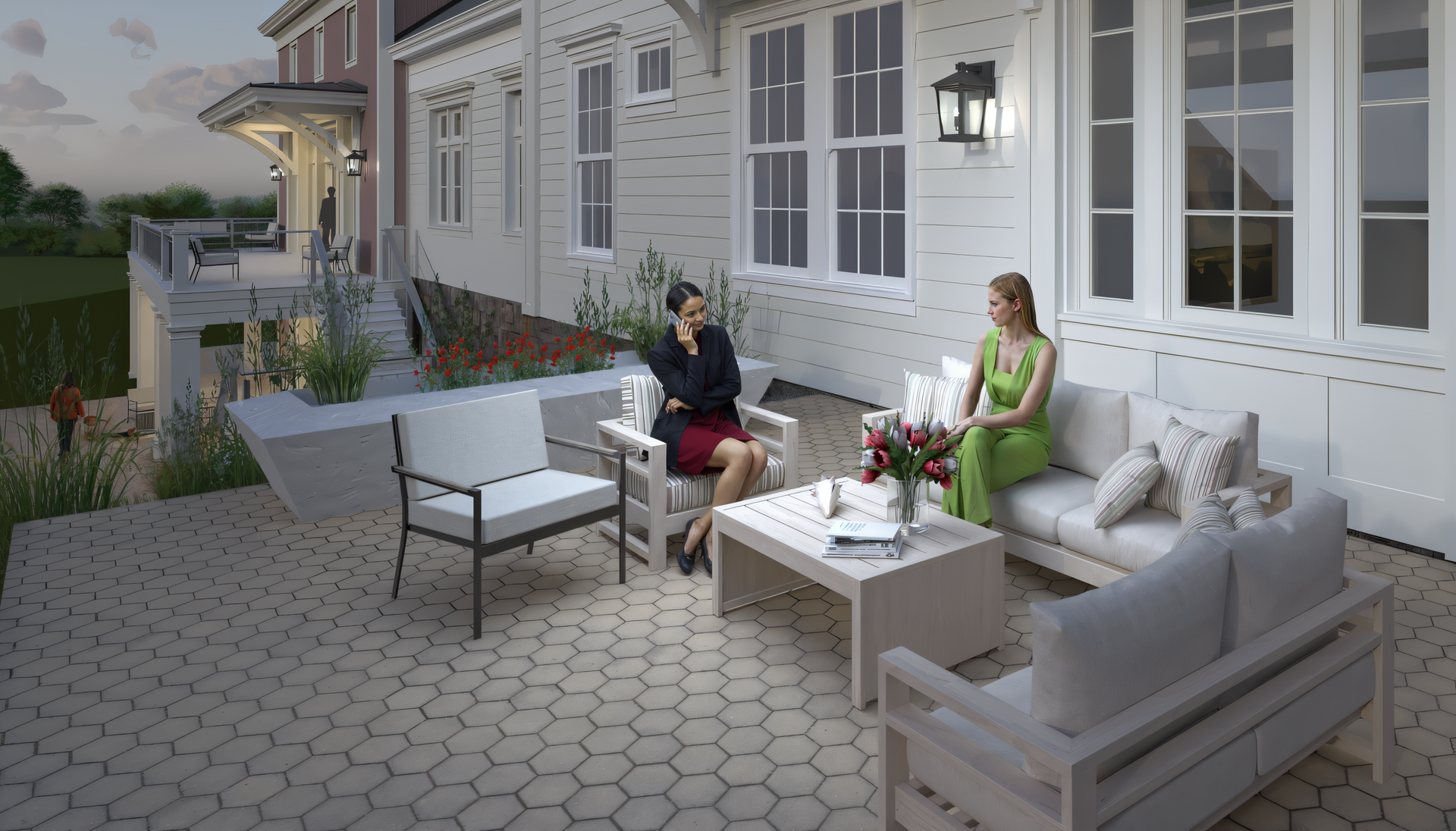 People chatting on a patio with gray outdoor seating beside a white house at dusk
