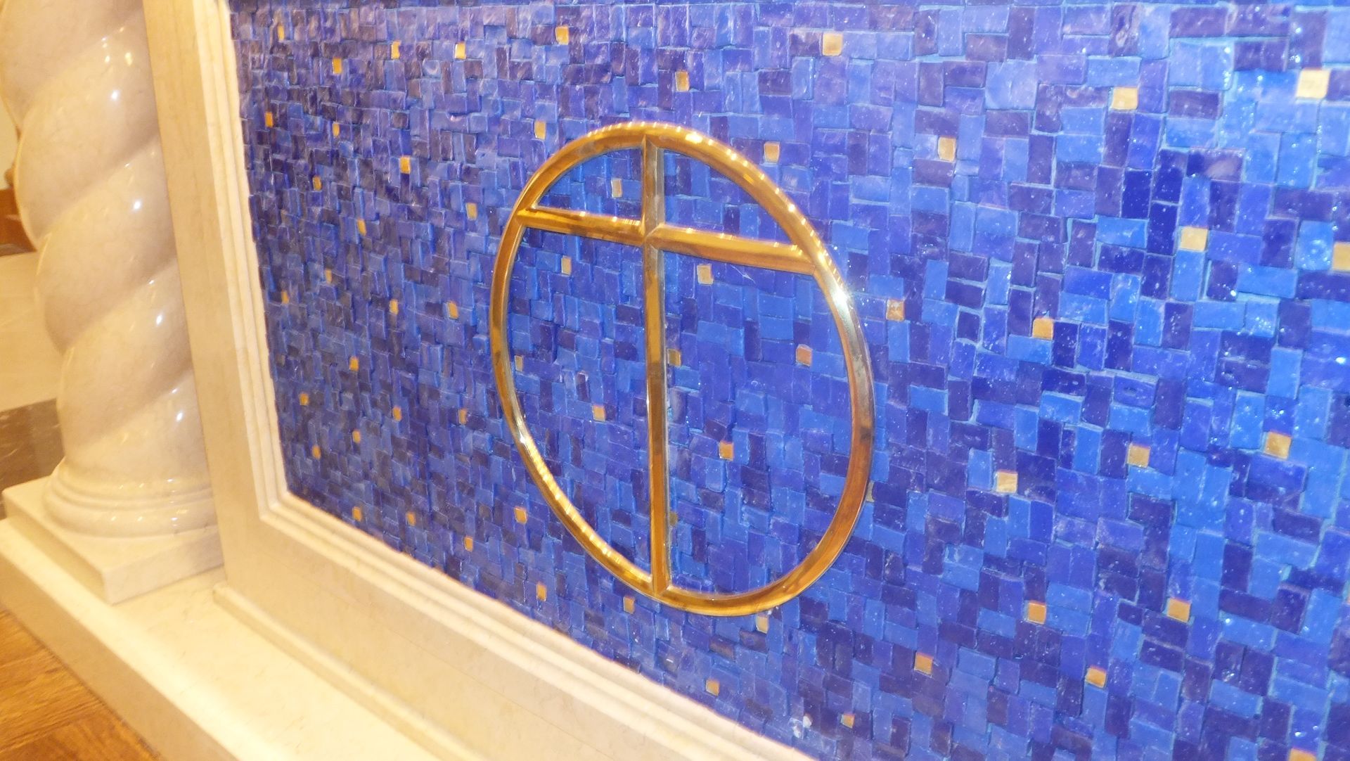 Gold cross within a circle on a blue mosaic wall.