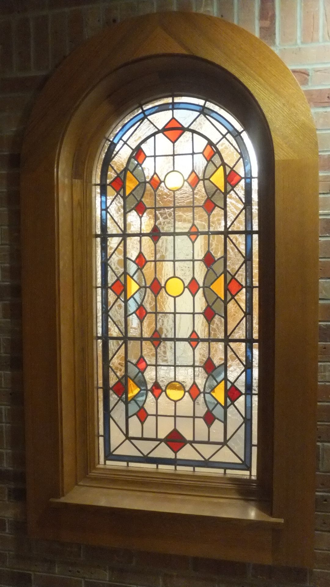 Stained glass window with red, yellow, and clear panes. Wooden frame set in a brick wall.