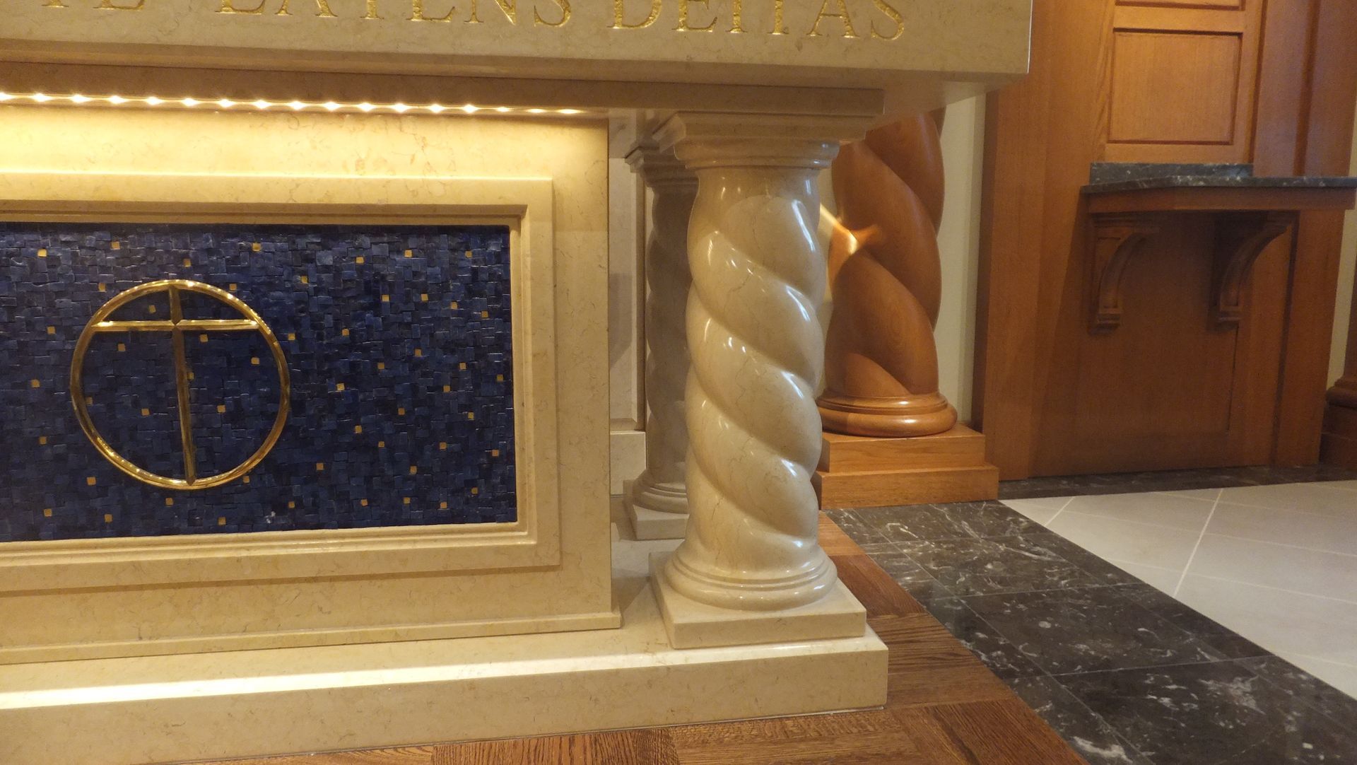 A church altar with a blue-tiled panel, gold cross, and twisted column.