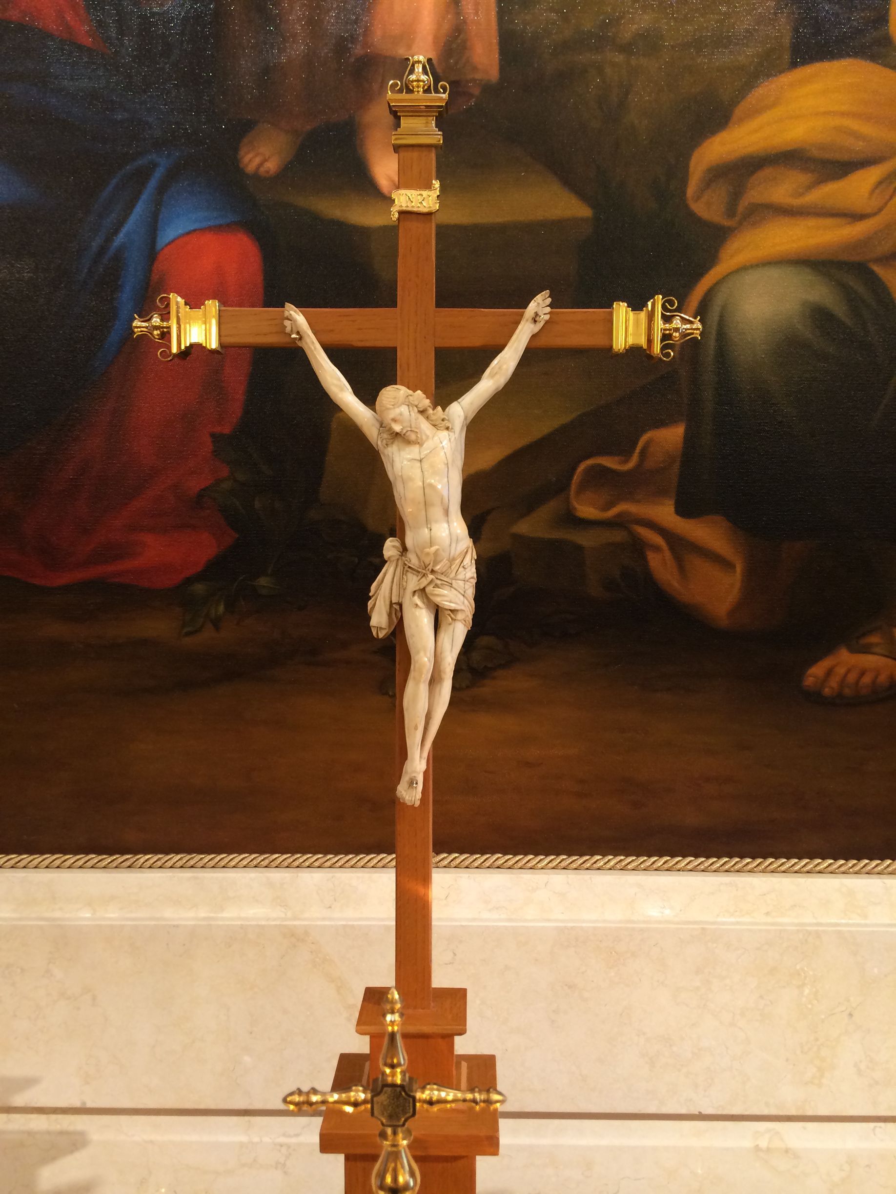 Crucifix with a sculpted white figure of Jesus on a wooden cross, against a backdrop of a painting.
