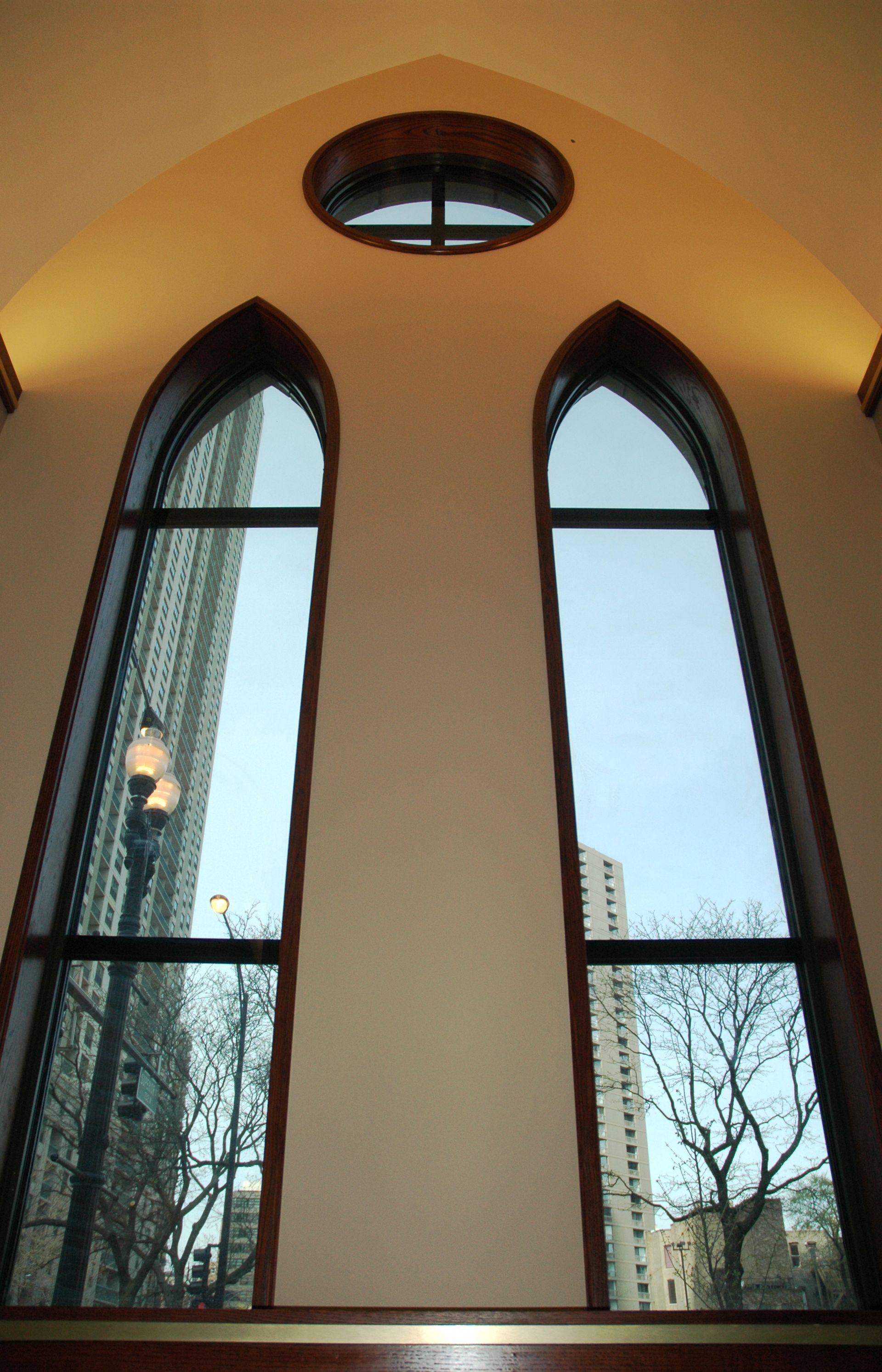 Two arched windows and a circular window above, reflecting city buildings.