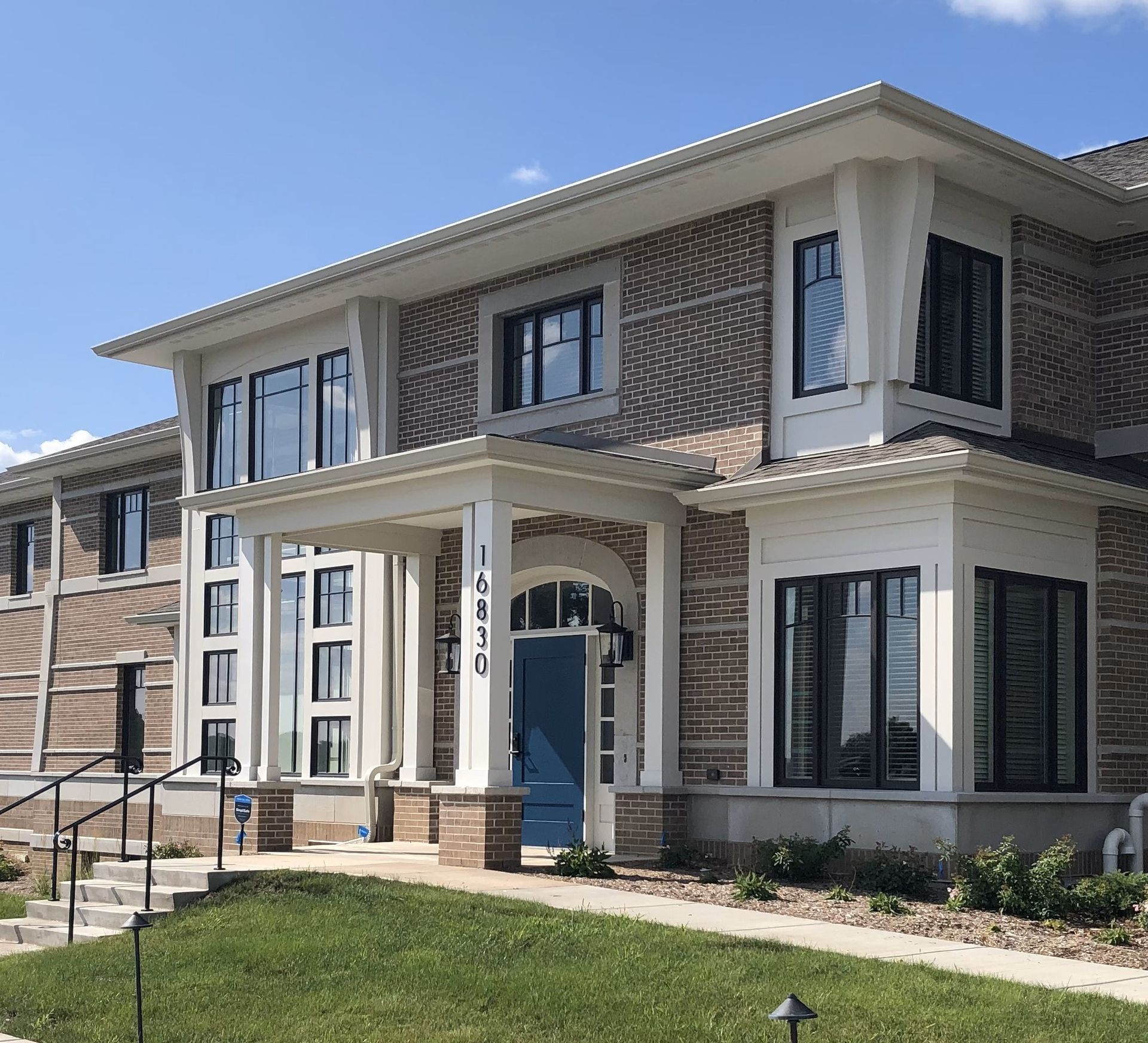 Two-story brick building with black-framed windows, a blue door, and a covered porch.