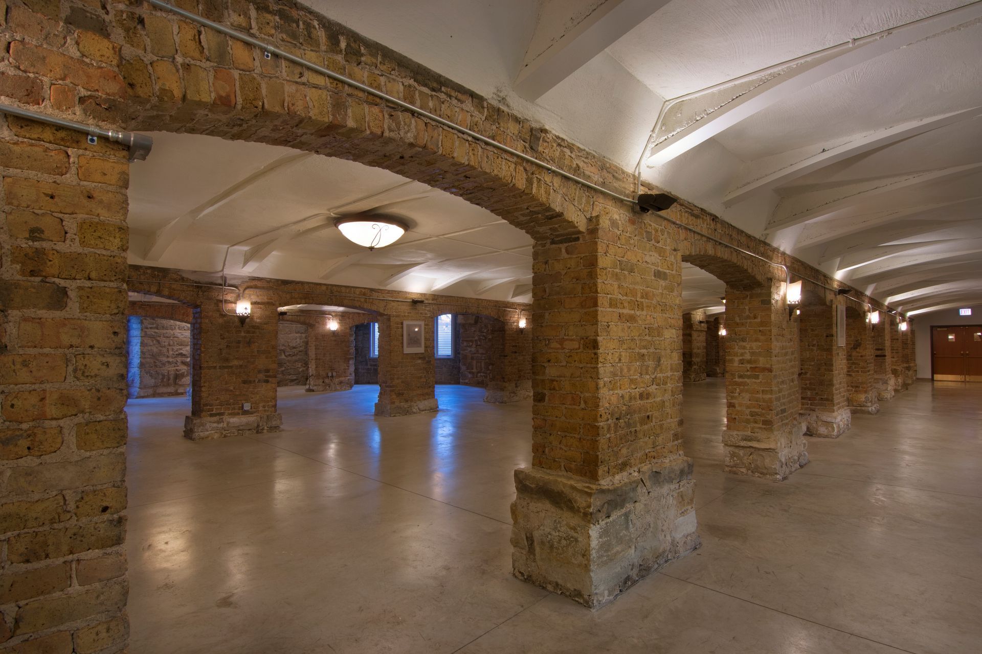 Open, arched brick columns in a large, bright hall with a polished concrete floor and overhead lighting.