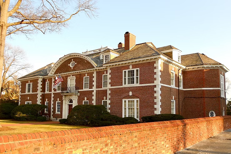 Brick mansion with white trim, red brick wall, flag on balcony, sunny day.