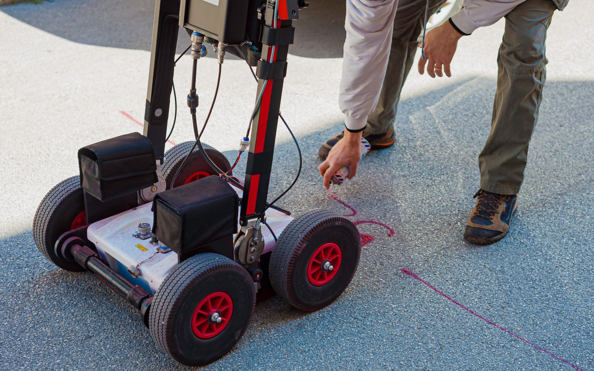 Man using GPR device for floor scanning on outdoor pavement in geophysical subsurface inspection.