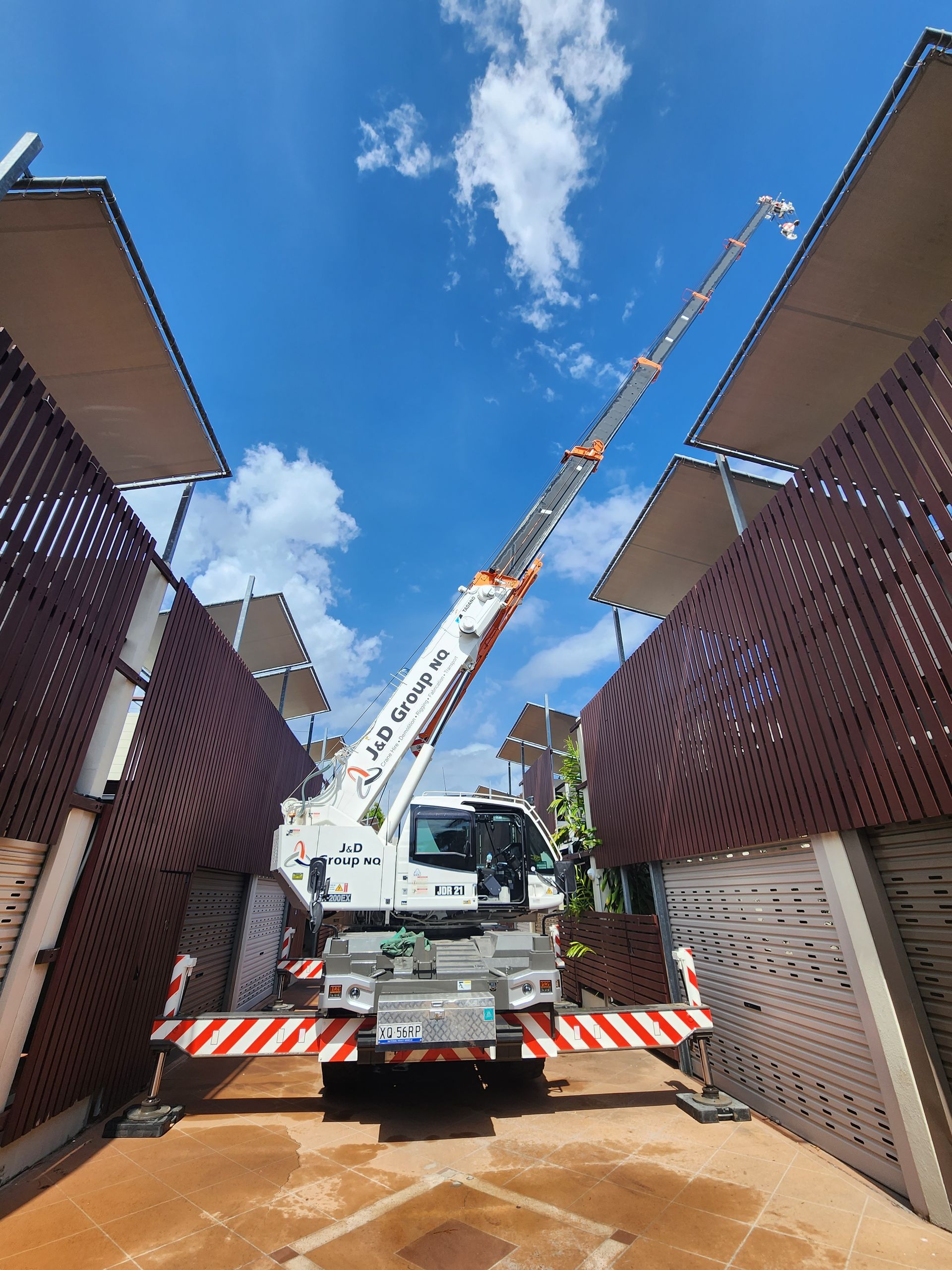 A Large Crane Is Parked In A Parking Lot Between Two Buildings — J & D Rigging Pty Ltd In Bohle, QLD